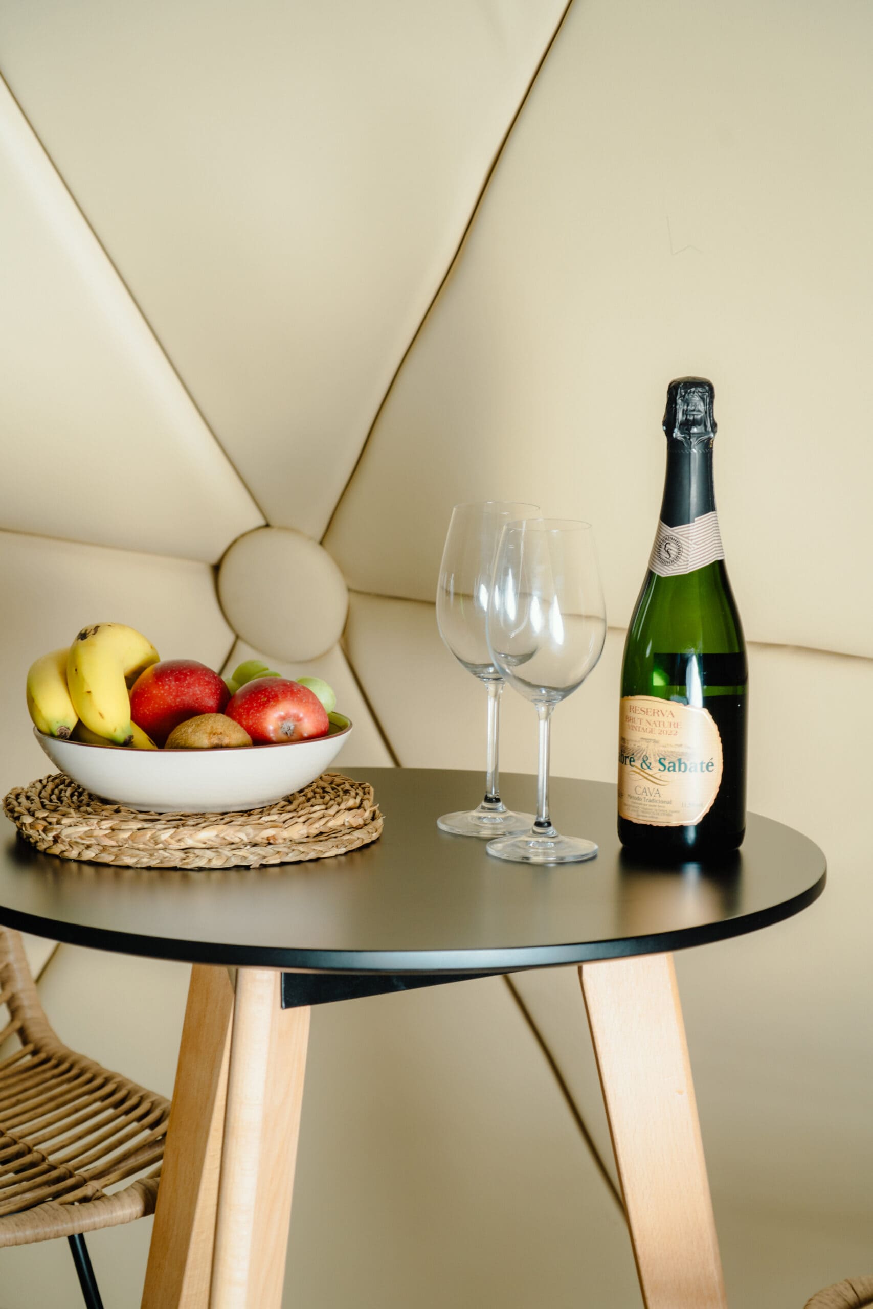 Botella de cava, copas y cesta de frutas frescas preparada como detalle de bienvenida sobre mesa en el interior del glamping