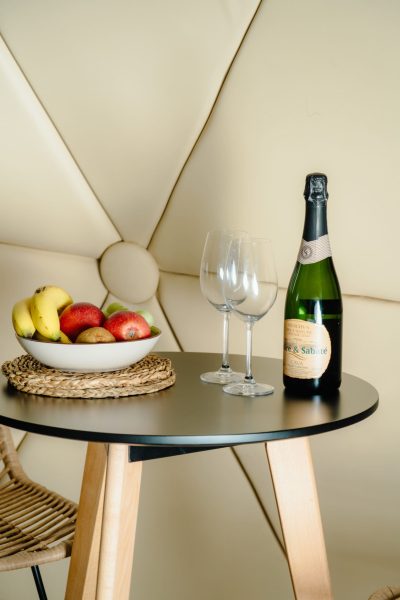 Botella de cava, copas y cesta de frutas frescas preparada como detalle de bienvenida sobre mesa en el interior del glamping